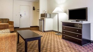 Une chambre d’hôtel avec un canapé, une petite table, un téléviseur posé sur une commode, un four à micro-ondes et une lampe.
