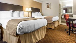 Une chambre d’hôtel avec deux lits, un bureau, une chaise et une salle de bain visible à travers une porte ouverte.