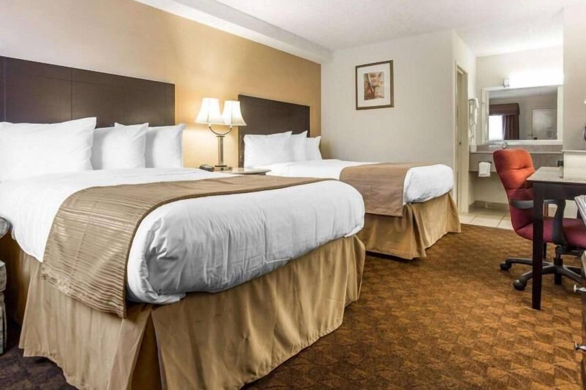 A hotel room with two beds, a desk, a chair, and a bathroom visible through an open door.