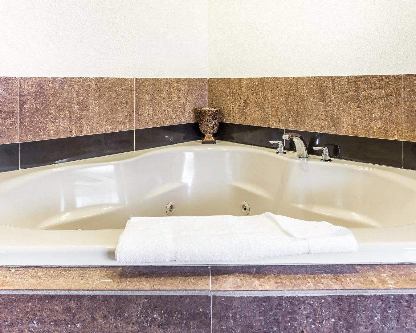 A large bathtub with two faucets and a decorative vase.