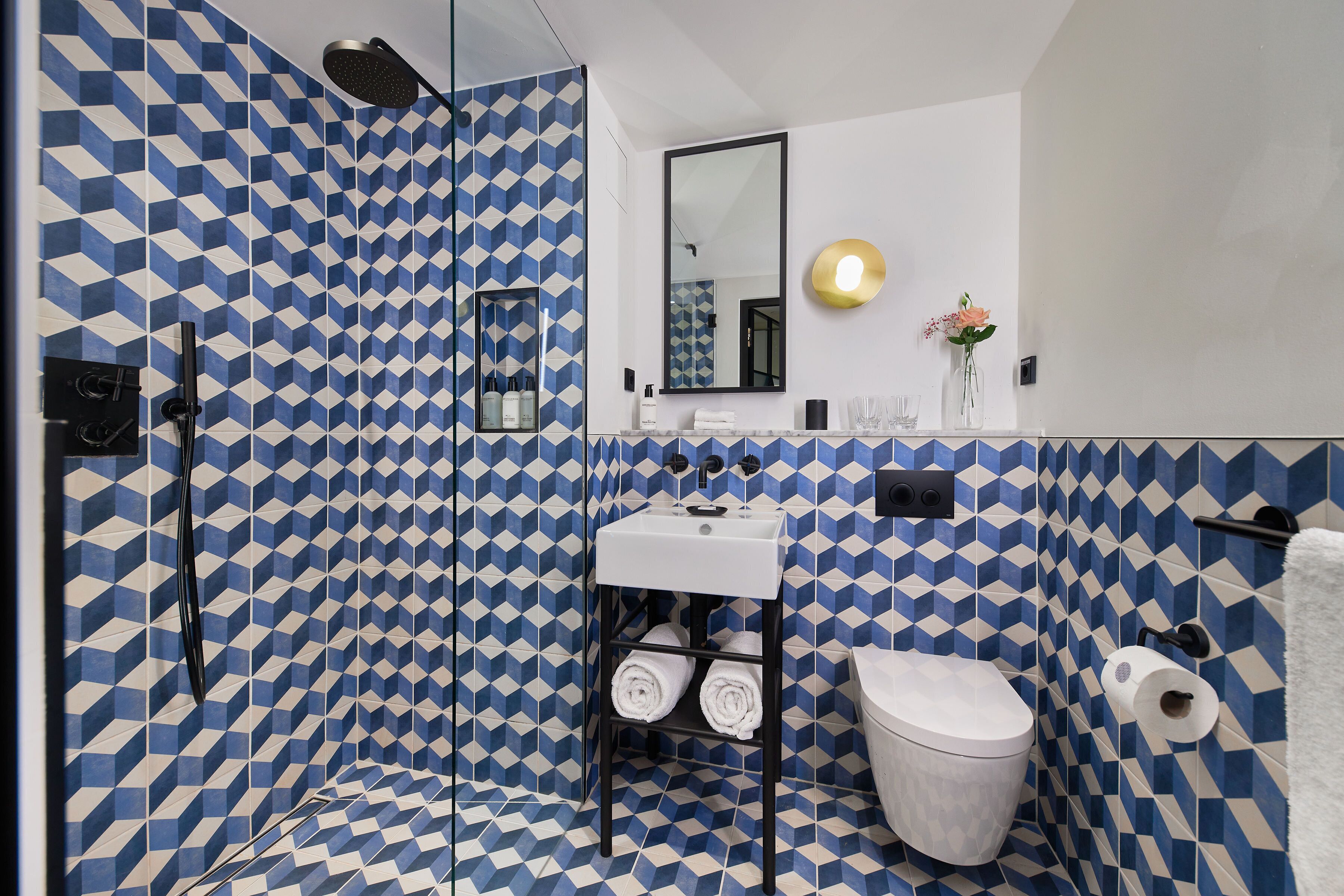 Une salle de bain avec un carrelage aux motifs géométriques, un lavabo blanc, des toilettes et une douche.