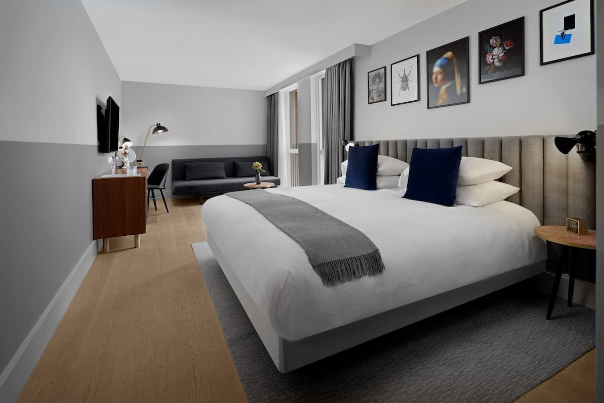 Ein modernes Hotelzimmer mit einem großen Bett, einem Schreibtisch, einer Sitzecke und Blick ins Freie.