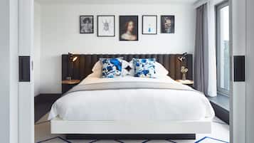 A modern bedroom with a large bed, a headboard with integrated lighting, a side table with a lamp, and a window with a view.