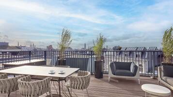 A rooftop terrace with a table, chairs, and potted plants.