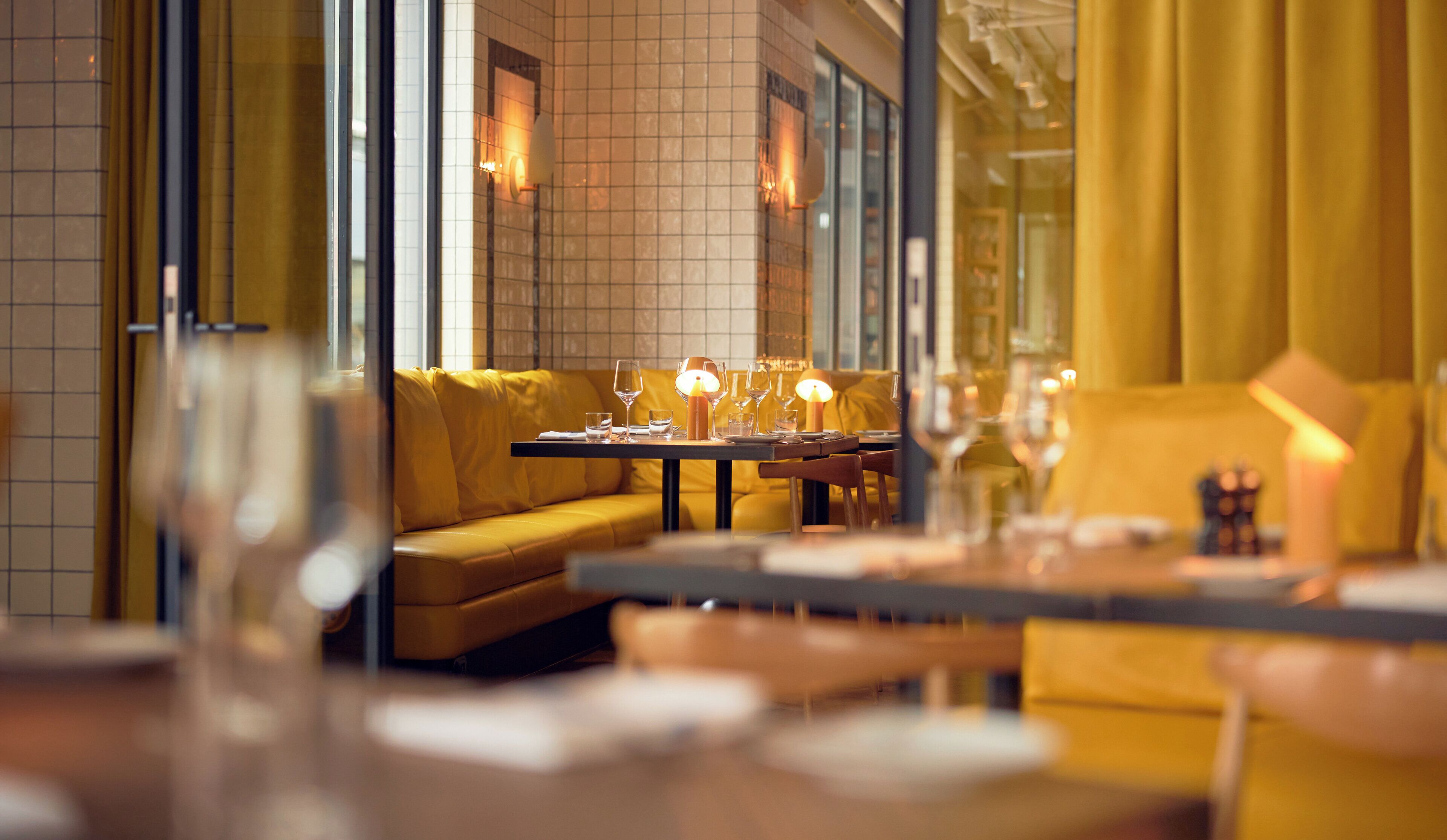 A restaurant interior with yellow seating, tables set with glasses and cutlery, and a modern design.