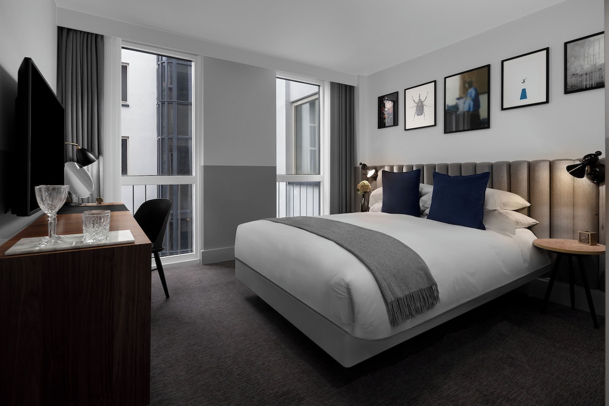 Une chambre d’hôtel moderne dotée d’un grand lit, d’un bureau avec une chaise, d’un téléviseur à écran plat et d’une fenêtre avec des rideaux.