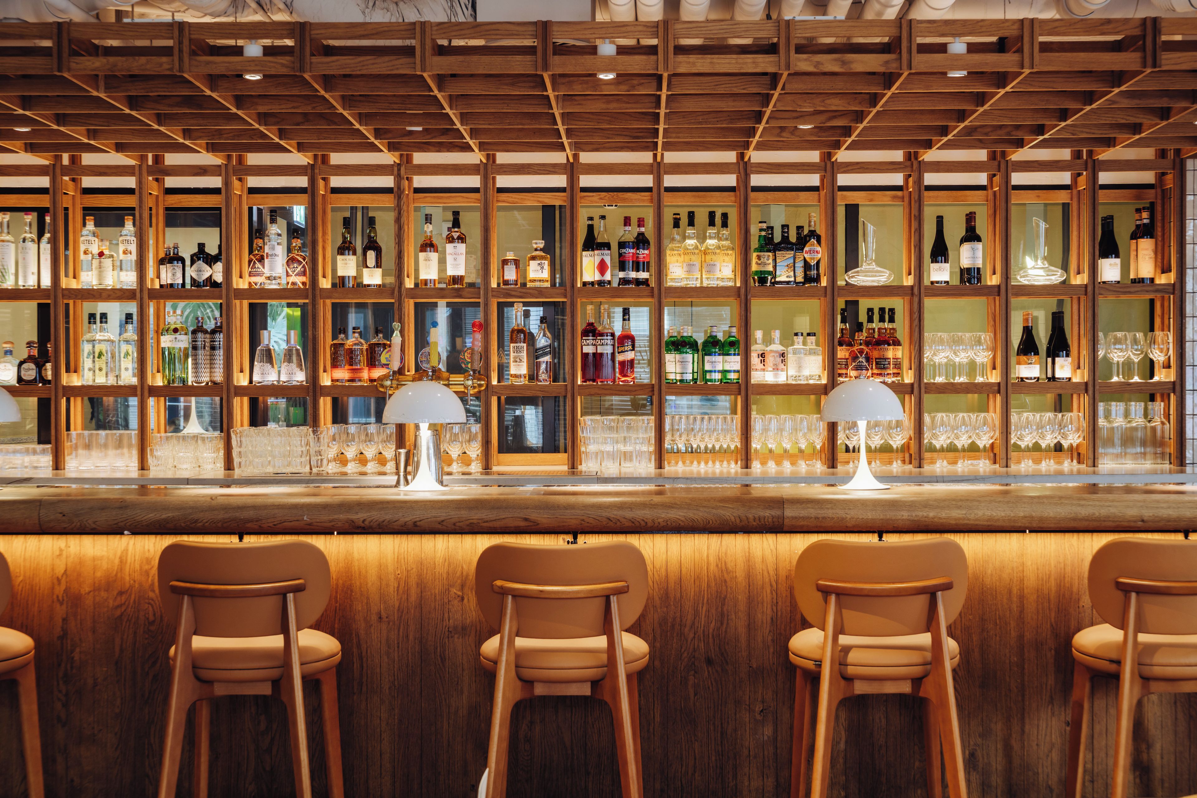 A bar area with wooden shelves displaying various bottles and glasses.