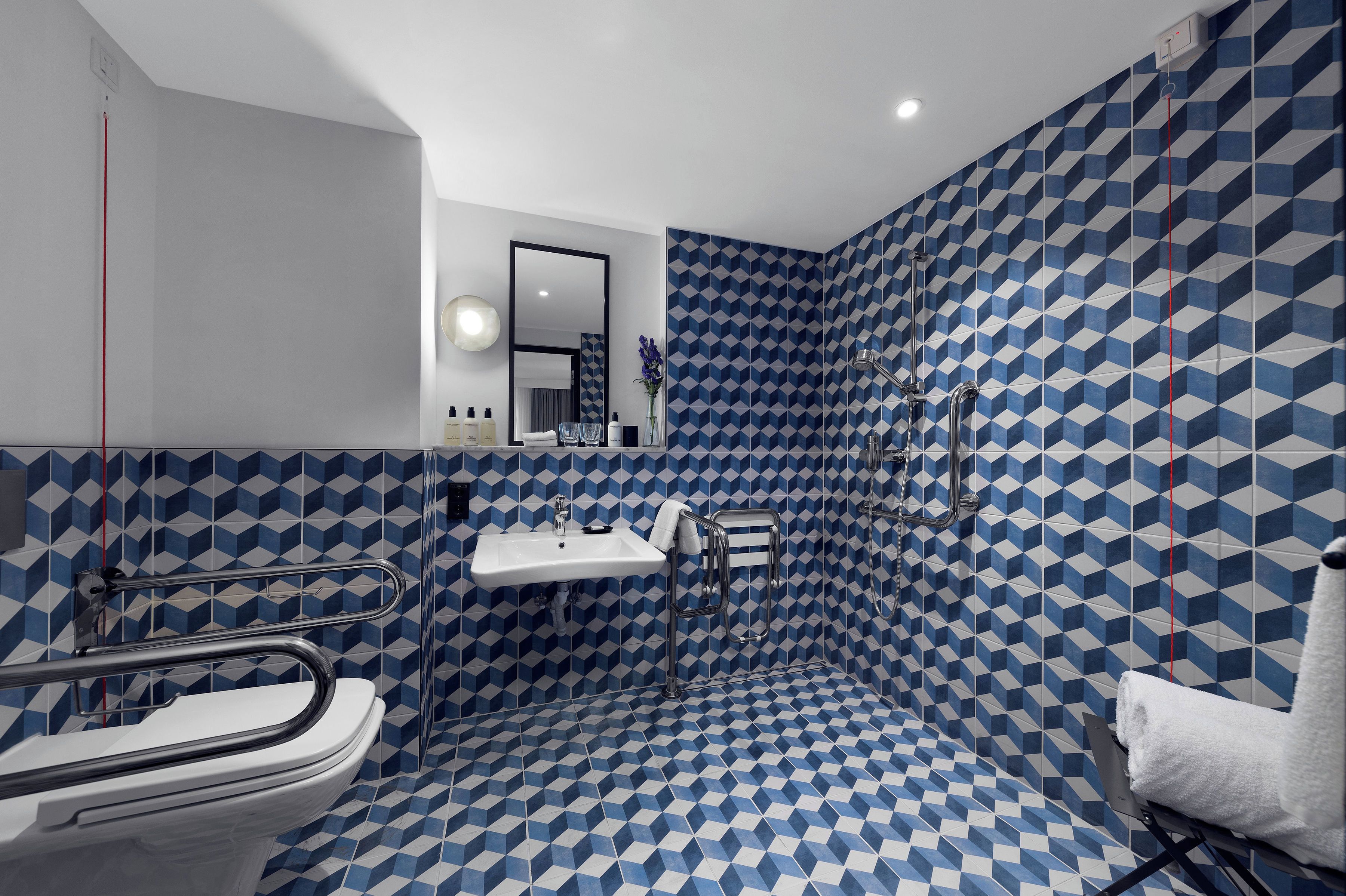 Un bagno con pavimento in piastrelle a motivi geometrici, un lavandino bianco, uno specchio e una cabina doccia.