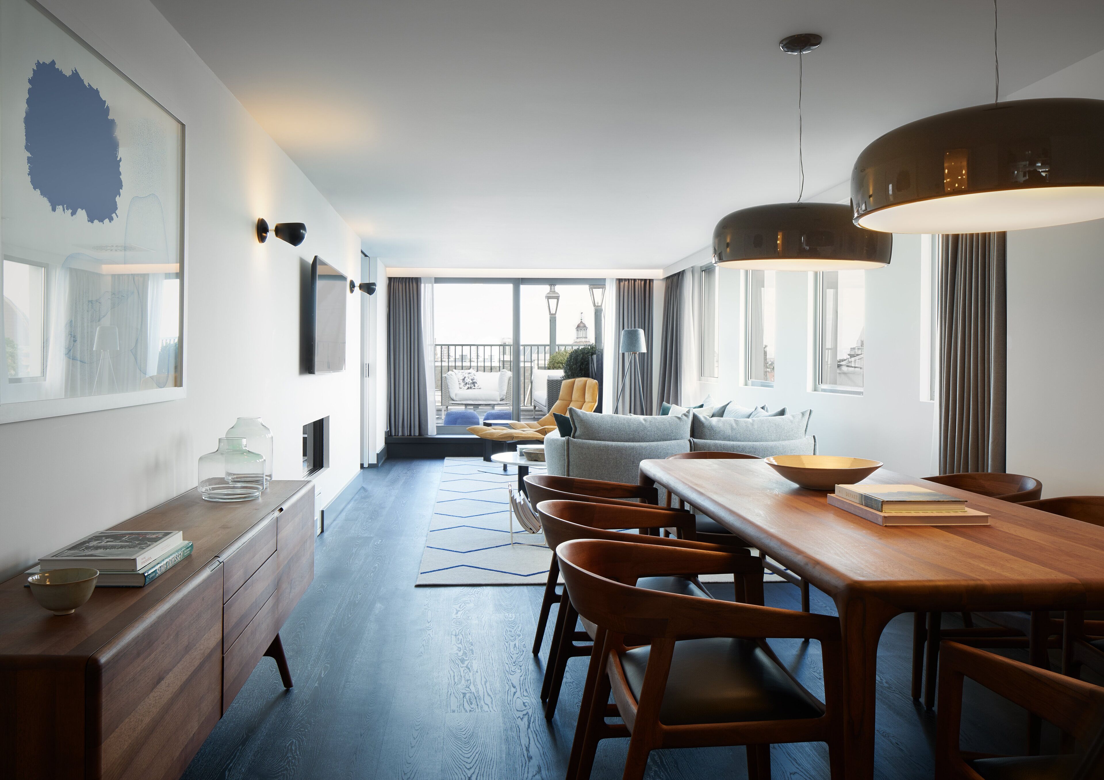 Ein modernes Hotelzimmer mit Essbereich, einer Sofagarnitur und Blick auf die Stadtlandschaft.