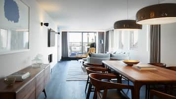 Ein modernes Hotelzimmer mit Essbereich, einer Sofagarnitur und Blick auf die Stadtlandschaft.