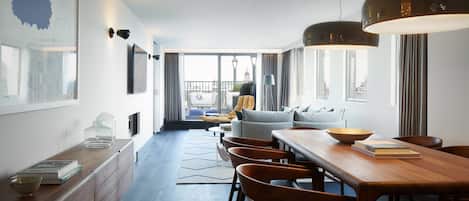 A modern hotel room with a dining area, a sofa set, and a view of the cityscape.