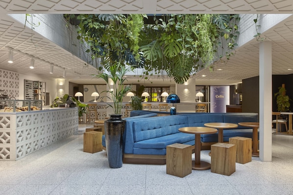 A modern lounge area with a blue sofa, wooden stools, and hanging plants.