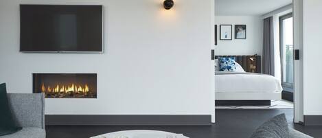 Habitación de hotel moderna con chimenea, una cama con almohada estampada en azul, un televisor de pantalla plana y vistas al exterior.