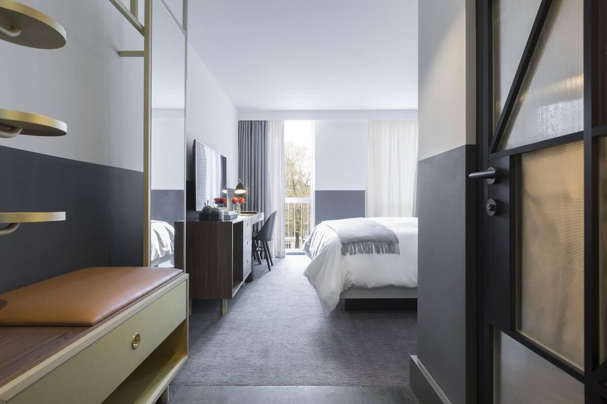 Ein Hotelzimmer mit Bett, Schreibtisch, Sessel, Kommode und einem großen Fenster.