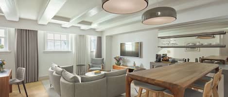 A modern living room with a wooden dining table, grey sofas, and a TV mounted on the wall.