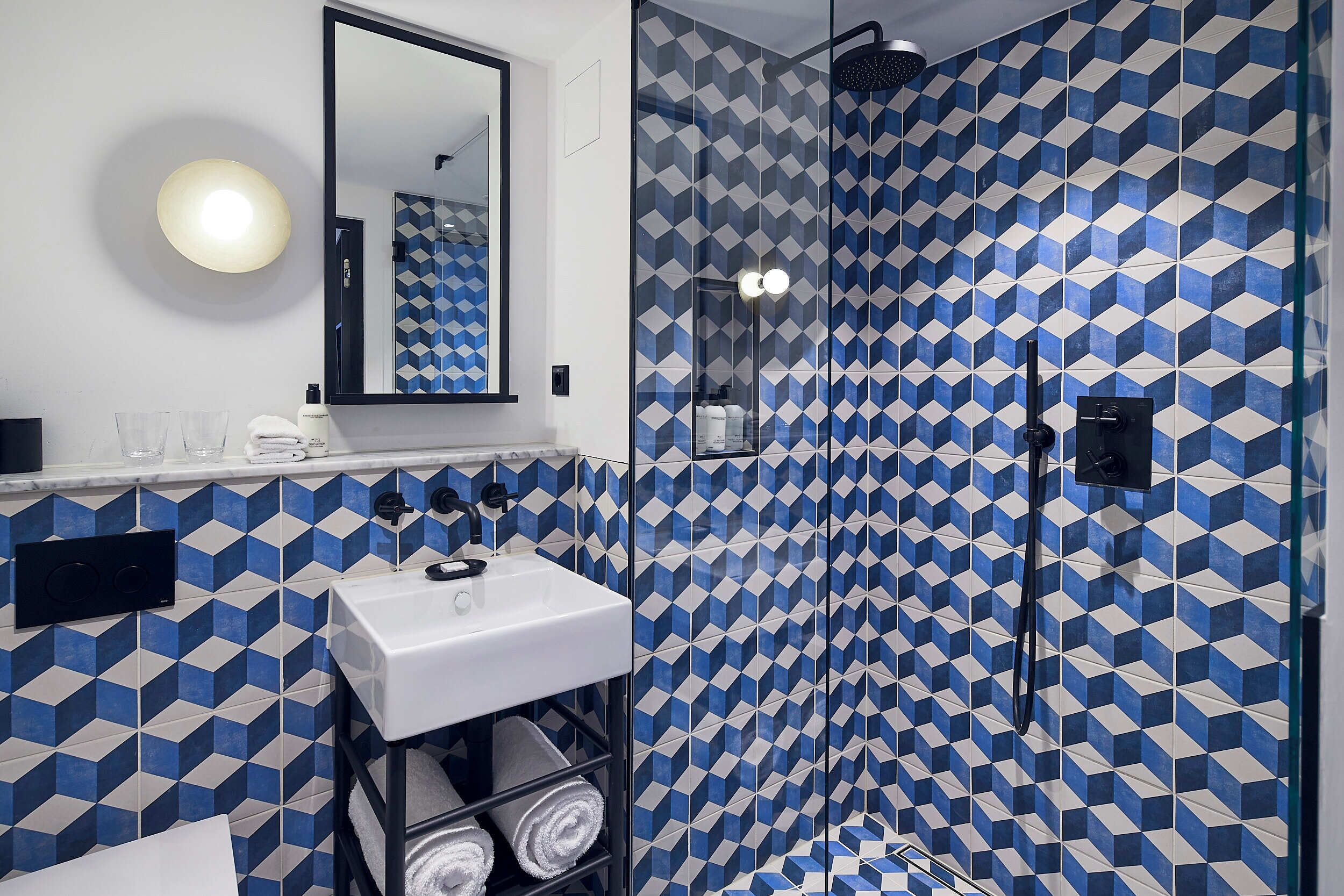 A bathroom with a geometric patterned wall, a white sink, a mirror, and a glass-enclosed shower area.