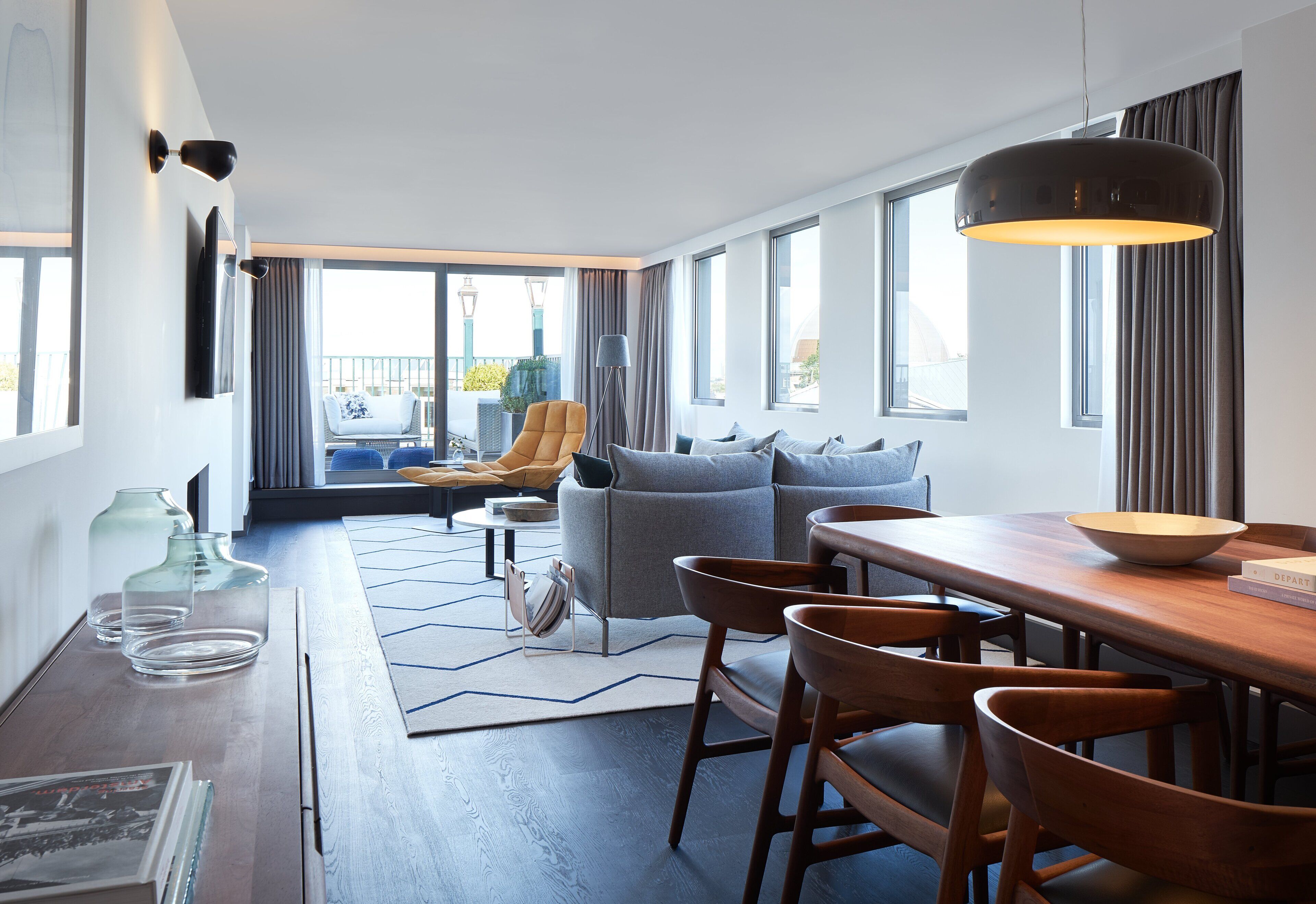 A modern hotel room with a dining area, a sofa, and a view of the city.