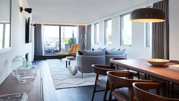 A modern hotel room with a dining area, a sofa, and a view of the city.