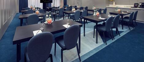 Ein Hotelkonferenzraum mit Tischen, Stühlen und einem Fernseher, der 'DeWitt Amsterdam' anzeigt.
