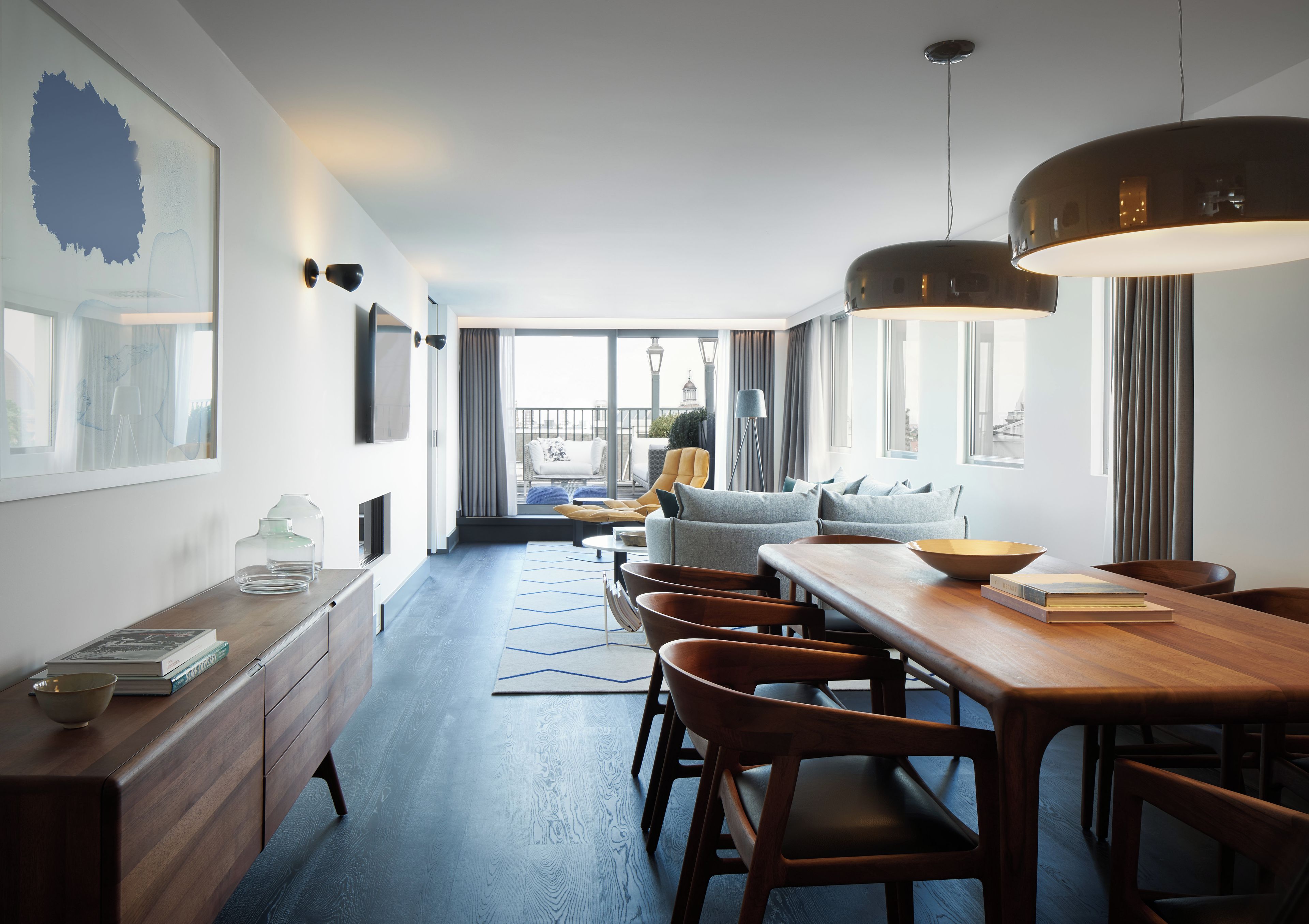 Habitación de hotel moderna con zona de comedor, sofá y vistas a la ciudad.