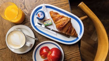 Bandeja de desayuno con un croissant, manzanas, un vaso de jugo de naranja, una taza de café y un recipiente pequeño de mantequilla.