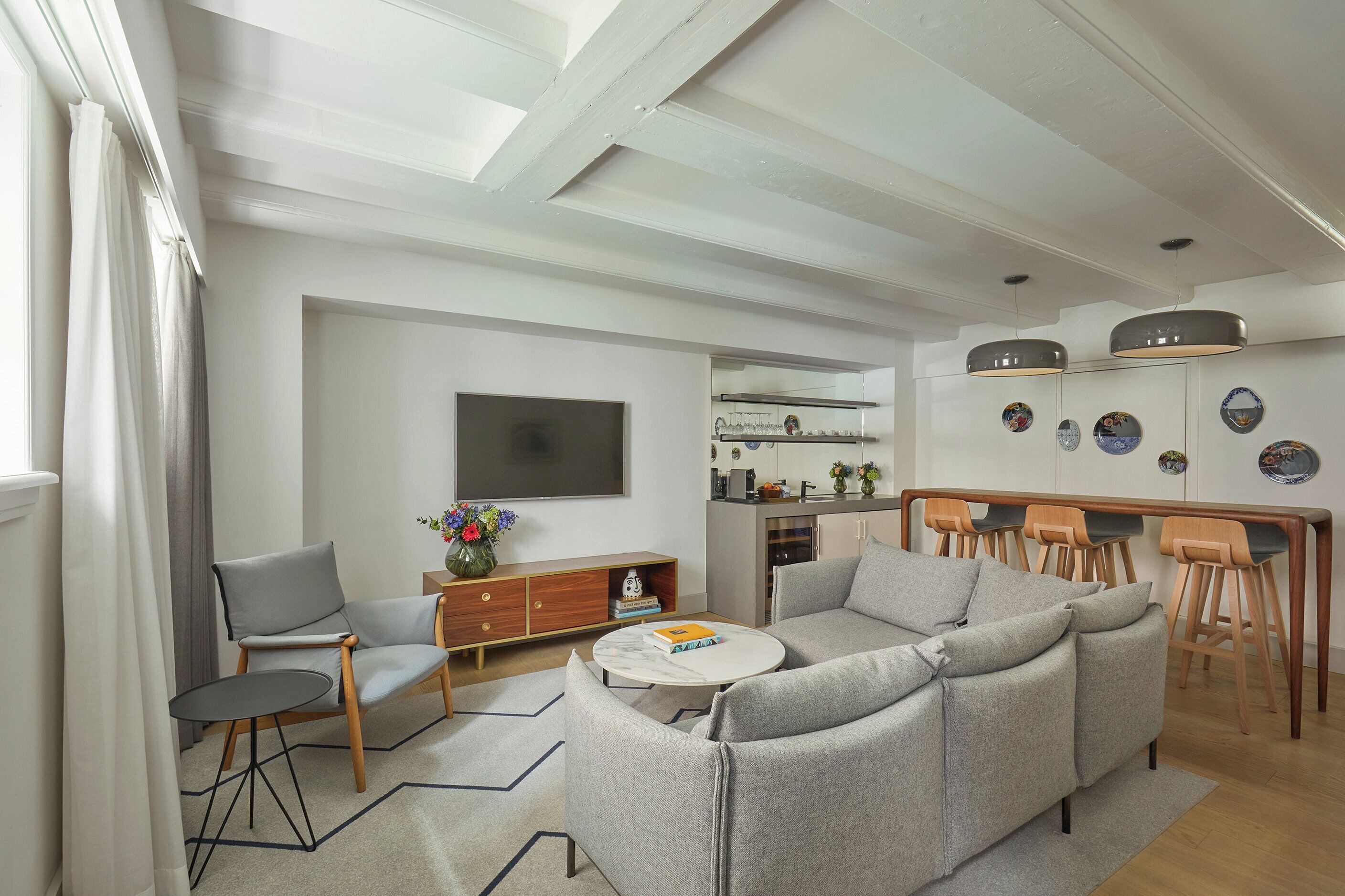 A modern living room with a sofa, a coffee table, and a TV. There is a kitchen area with a dining table and chairs.