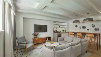 A modern living room with a sofa, a coffee table, and a TV. There is a kitchen area with a dining table and chairs.