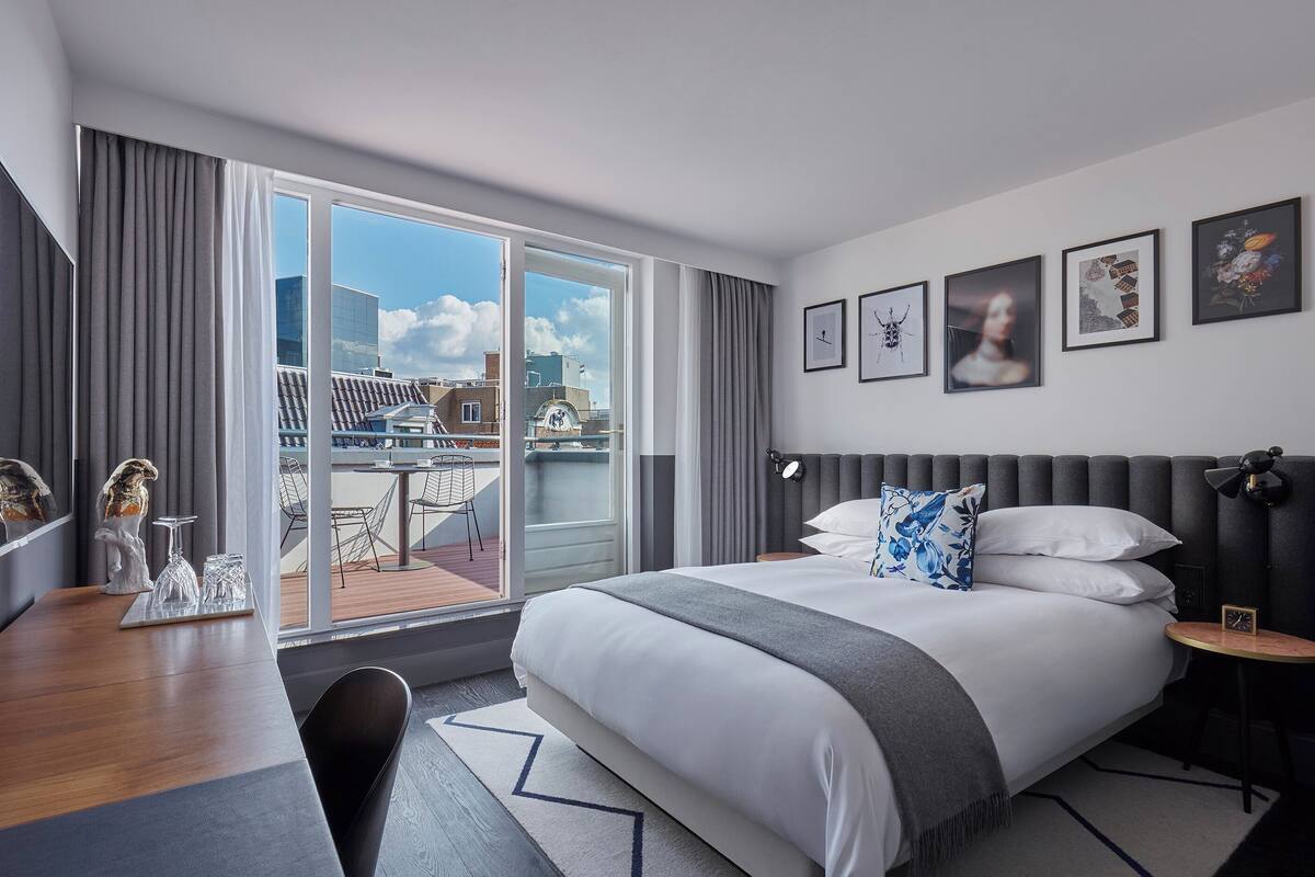 Ein modernes Hotelzimmer mit einem großen Bett, einem Schreibtisch und einem Balkon mit Blick auf die Stadt.