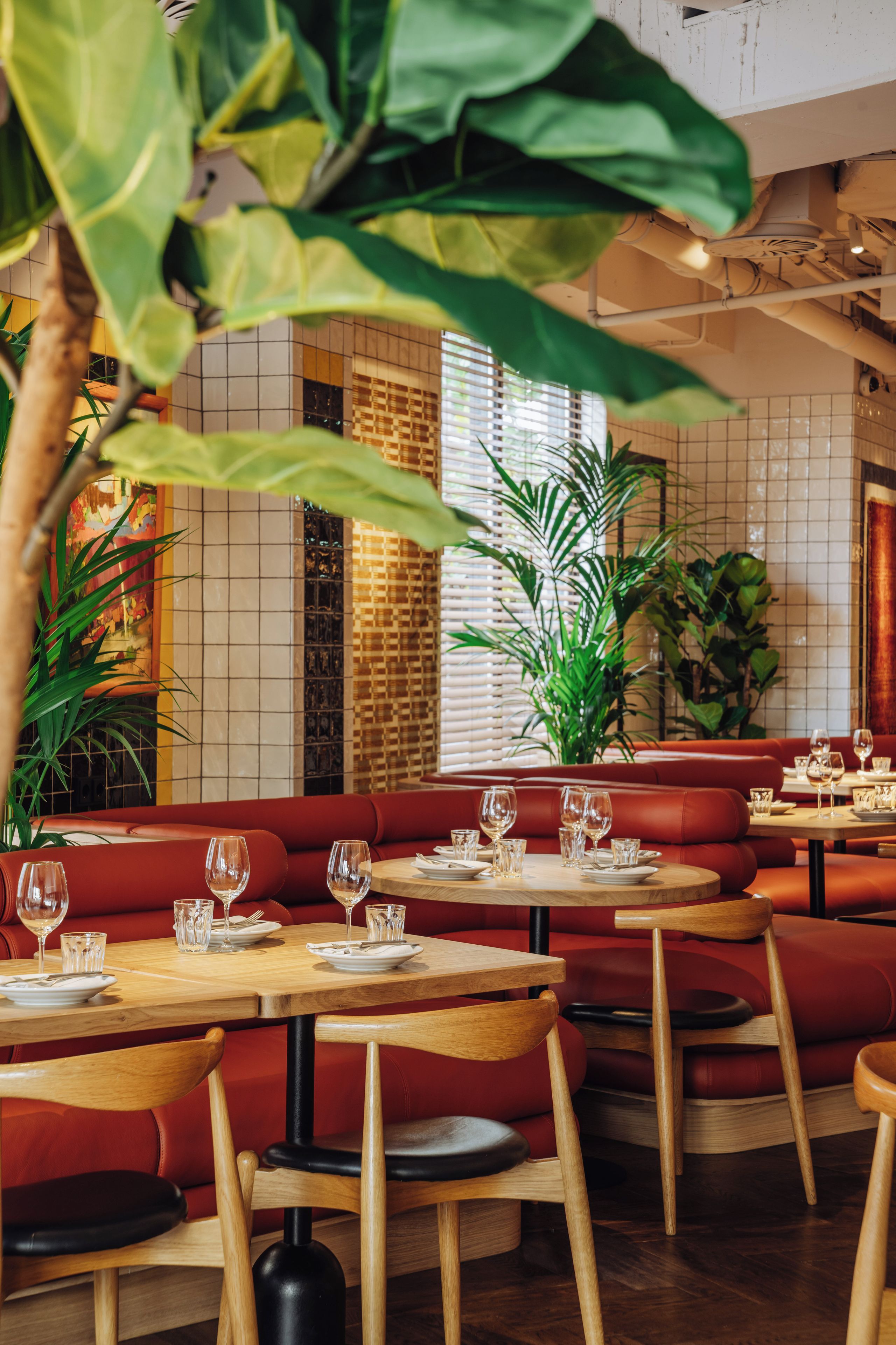 L’intérieur d’un restaurant avec des banquettes rouges, des tables en bois et des plantes en pot.