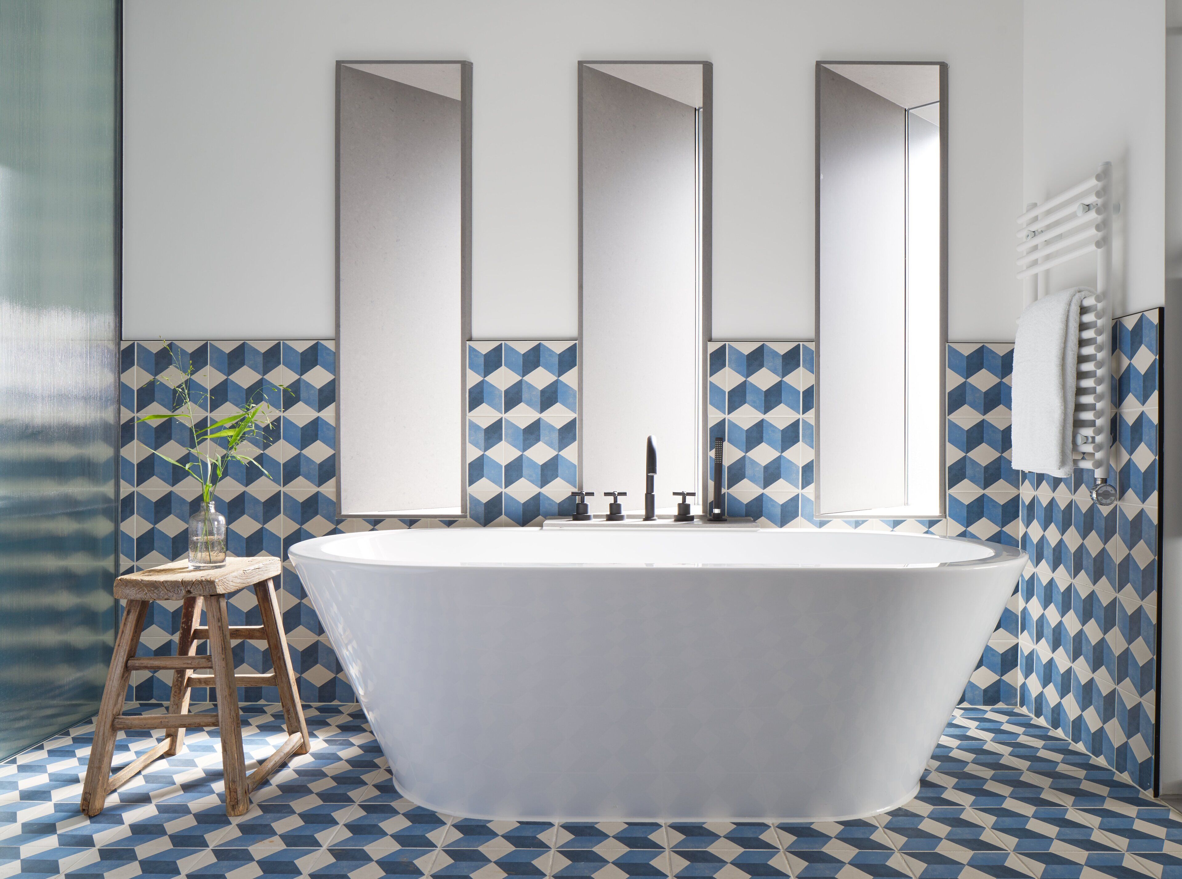 A bathroom with a freestanding bathtub, a wooden stool, and a mirror above the tub.