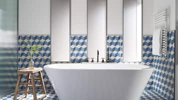 A bathroom with a freestanding bathtub, a wooden stool, and a mirror above the tub.