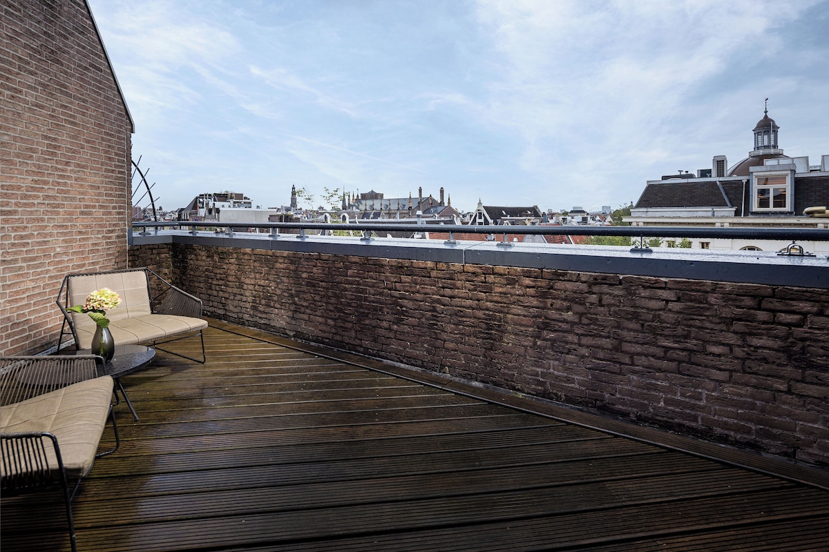 Une terrasse sur le toit, avec un mur en briques, une plateforme en bois et une vue sur les bâtiments en arrière-plan.