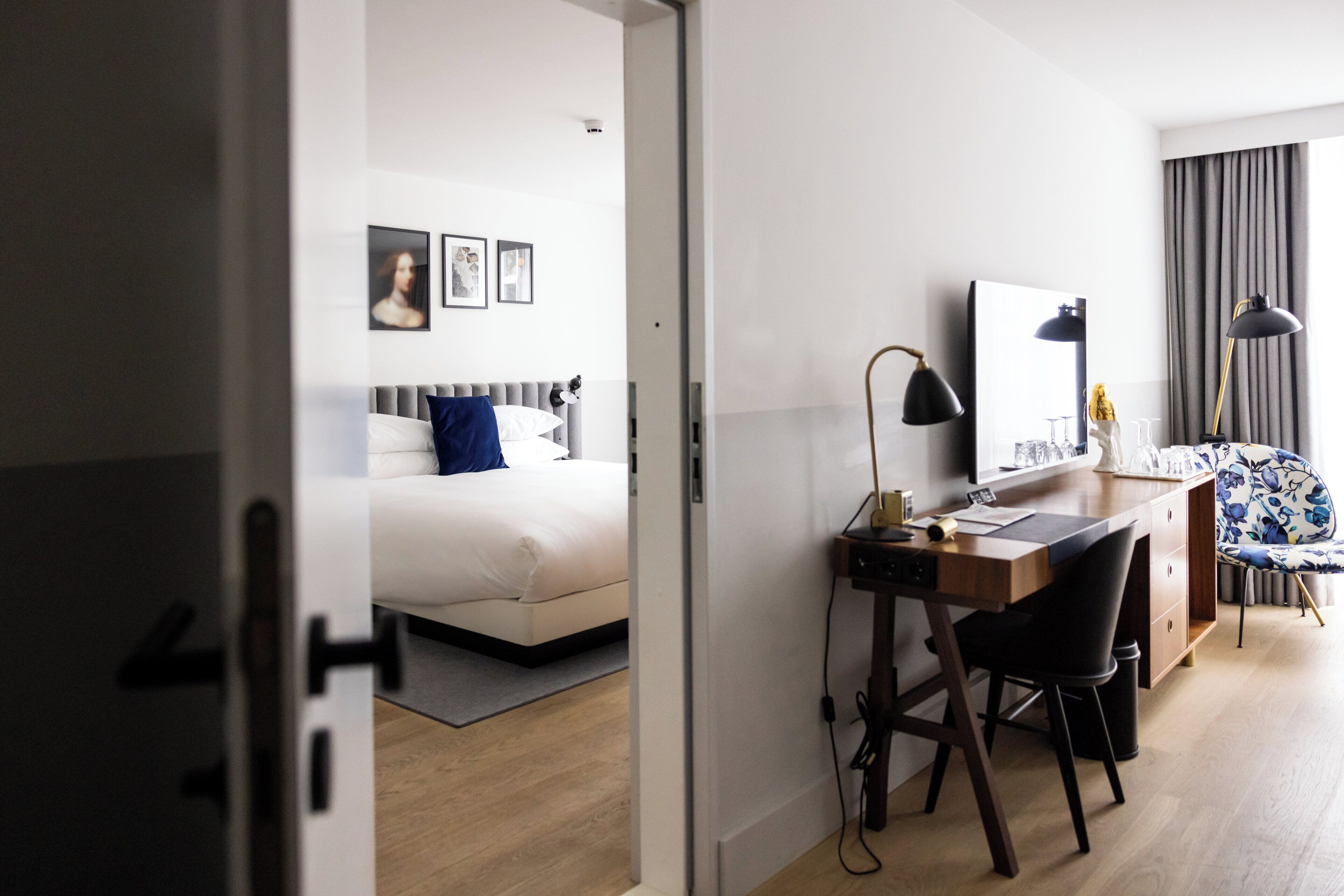 A modern hotel room with a bed, desk, chair, and a large mirror.