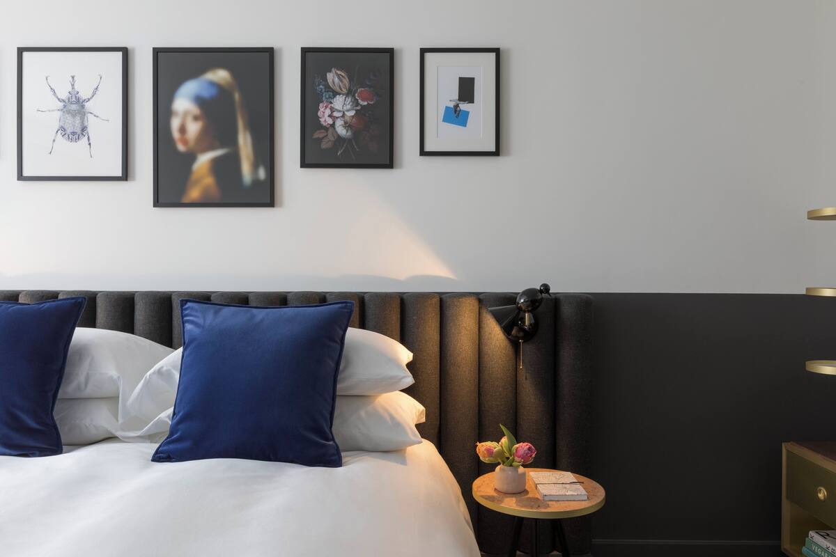 Ein modernes Hotelzimmer mit einem Bett, Kissen, einem Nachttisch, einer Lampe und drei gerahmten Kunstwerken an der Wand.