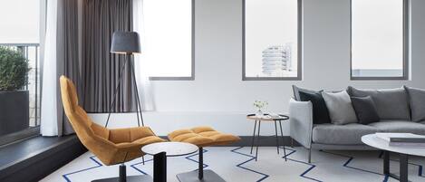 Un salon moderne comprenant un canapé, un fauteuil et un pouf, une petite table ronde et une lampe sur pied.