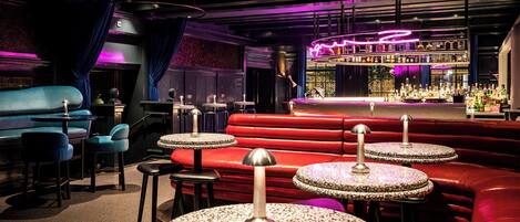 A bar area with red seating, a bar counter, and a variety of bottles.