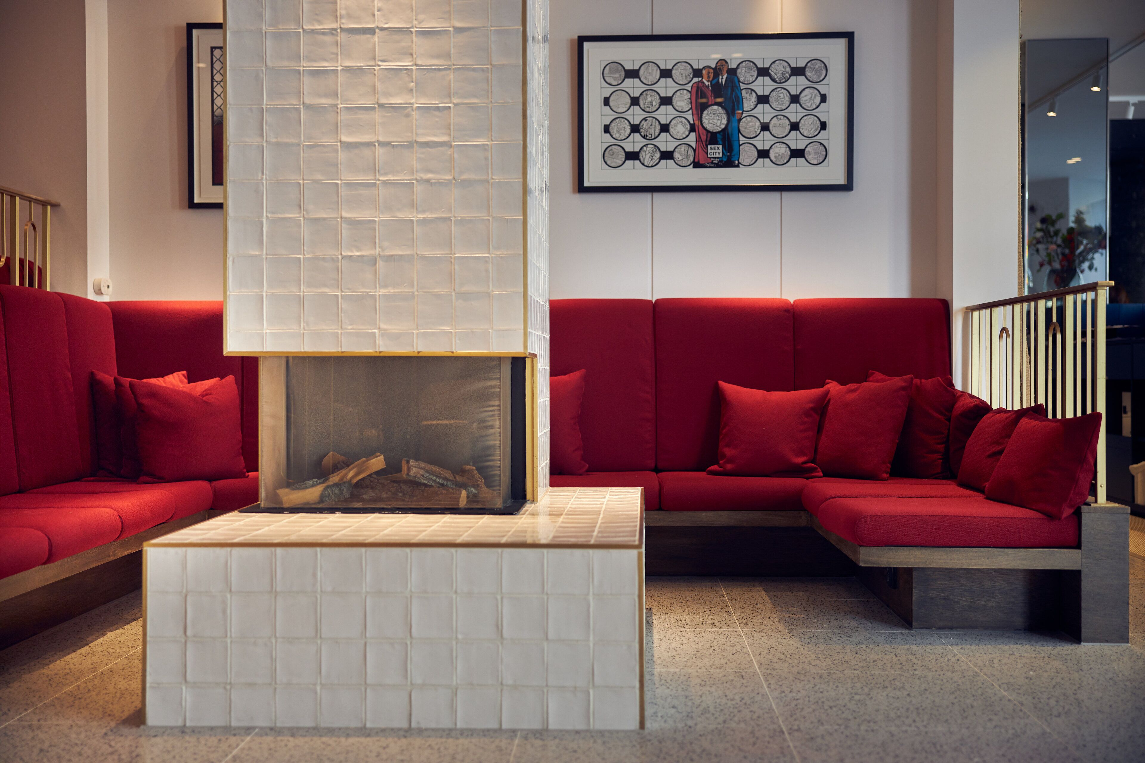 Una sala de estar moderna con un sofá rojo, una chimenea con azulejos blancos y una obra de arte abstracta enmarcada en la pared.