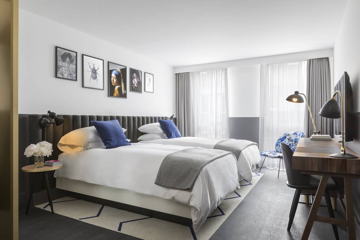Ein modernes Hotelzimmer mit zwei Betten, einem Schreibtisch und einem Fernseher.