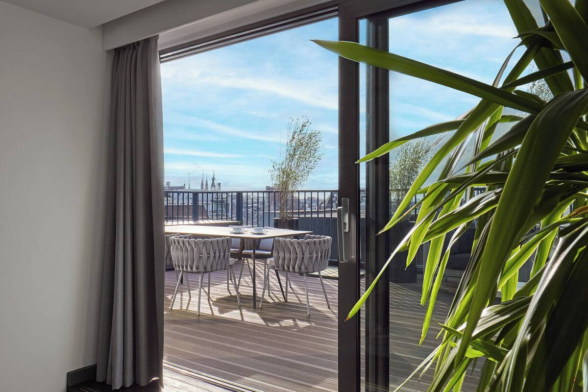 Ein modernes Zimmer mit einer Schiebeglastür, die auf einen Außenbalkon mit Esstisch und Stühlen führt.