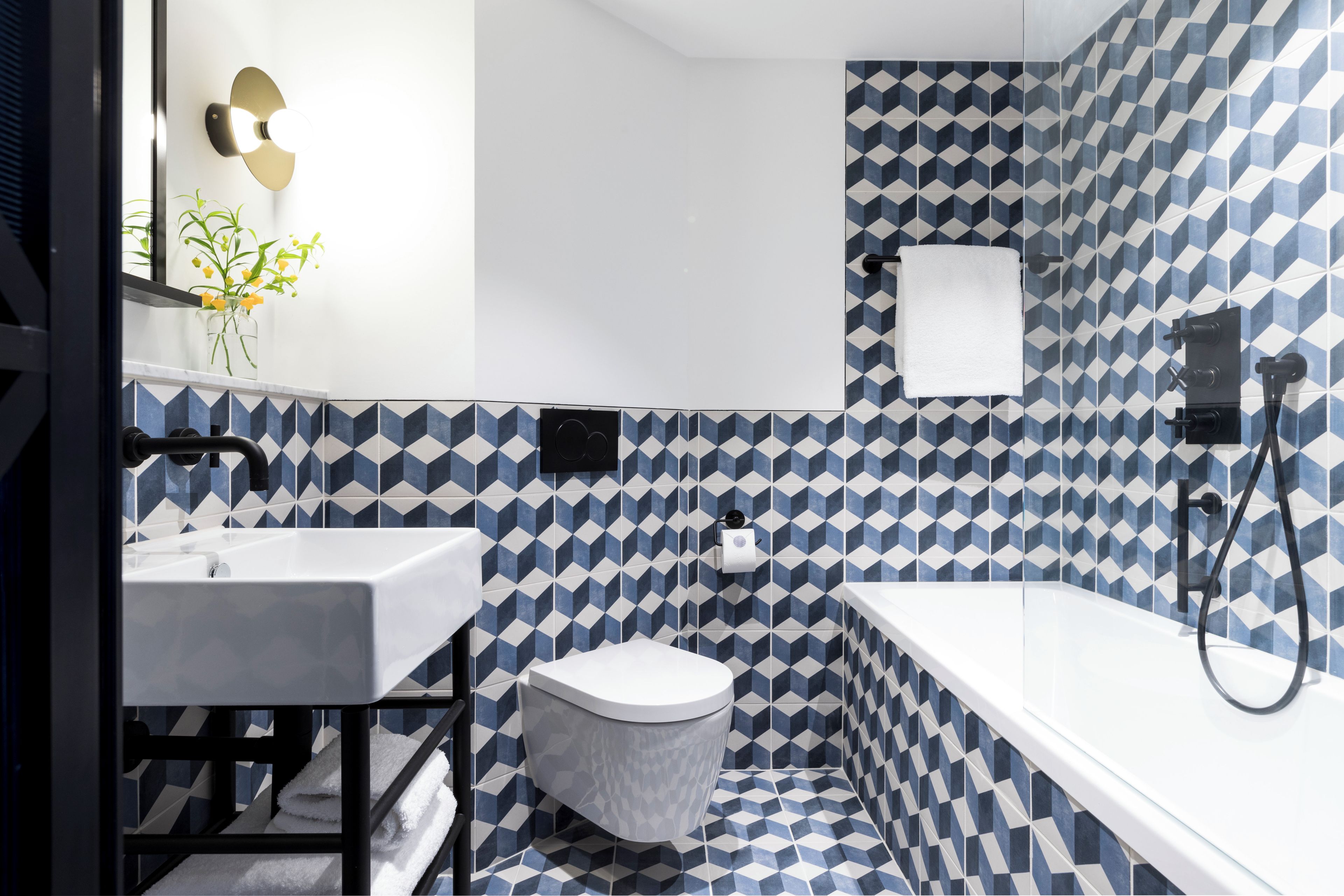 A modern bathroom with a geometric tile pattern, a white sink, a toilet, and a bathtub.