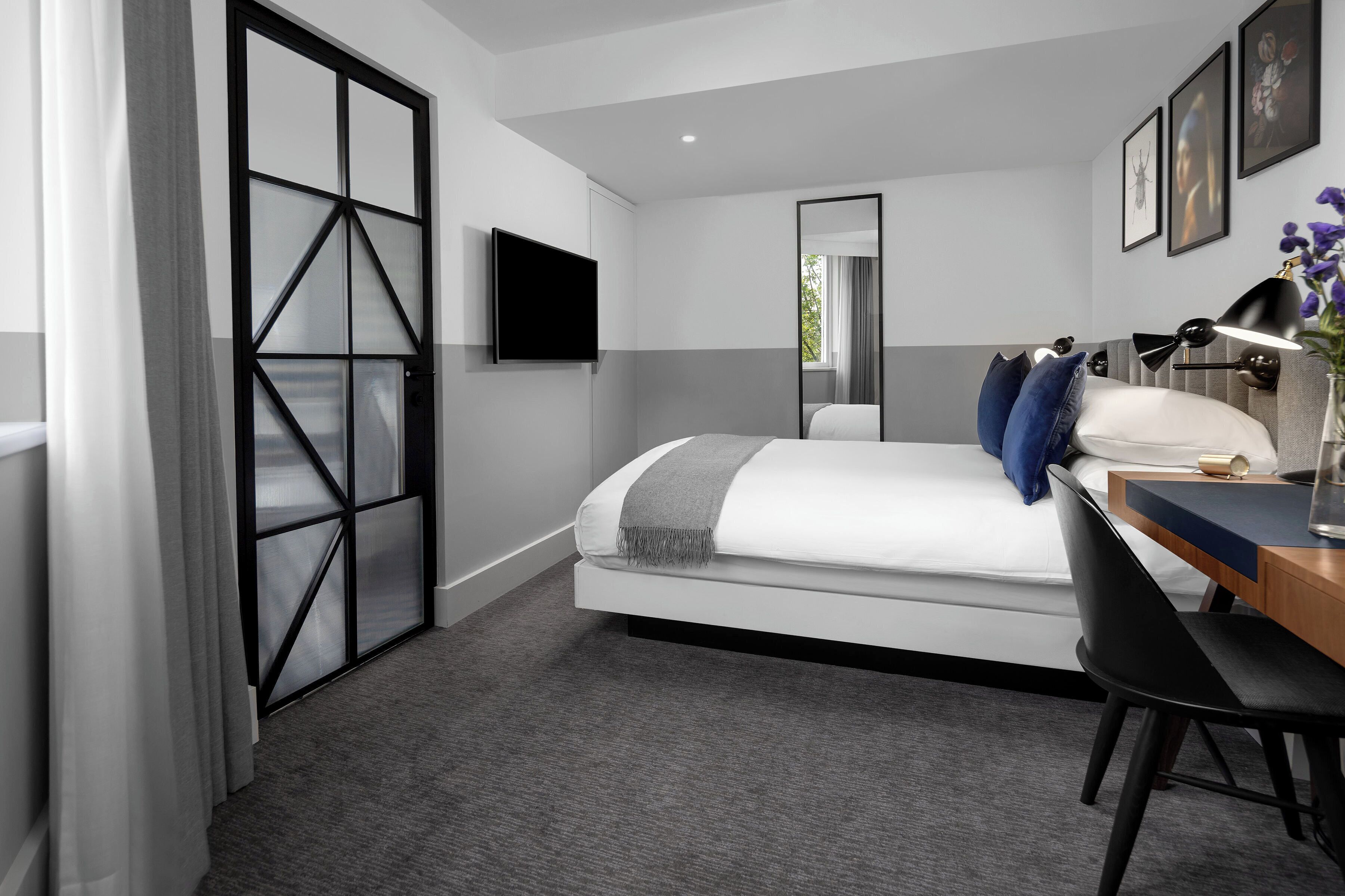 Une chambre d’hôtel moderne équipée d’un lit, d’un bureau, d’une chaise, d’une télévision et d’une grande fenêtre.