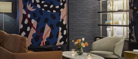 A modern lounge with a large abstract painting, leather seating, a round coffee table, and a bookshelf.