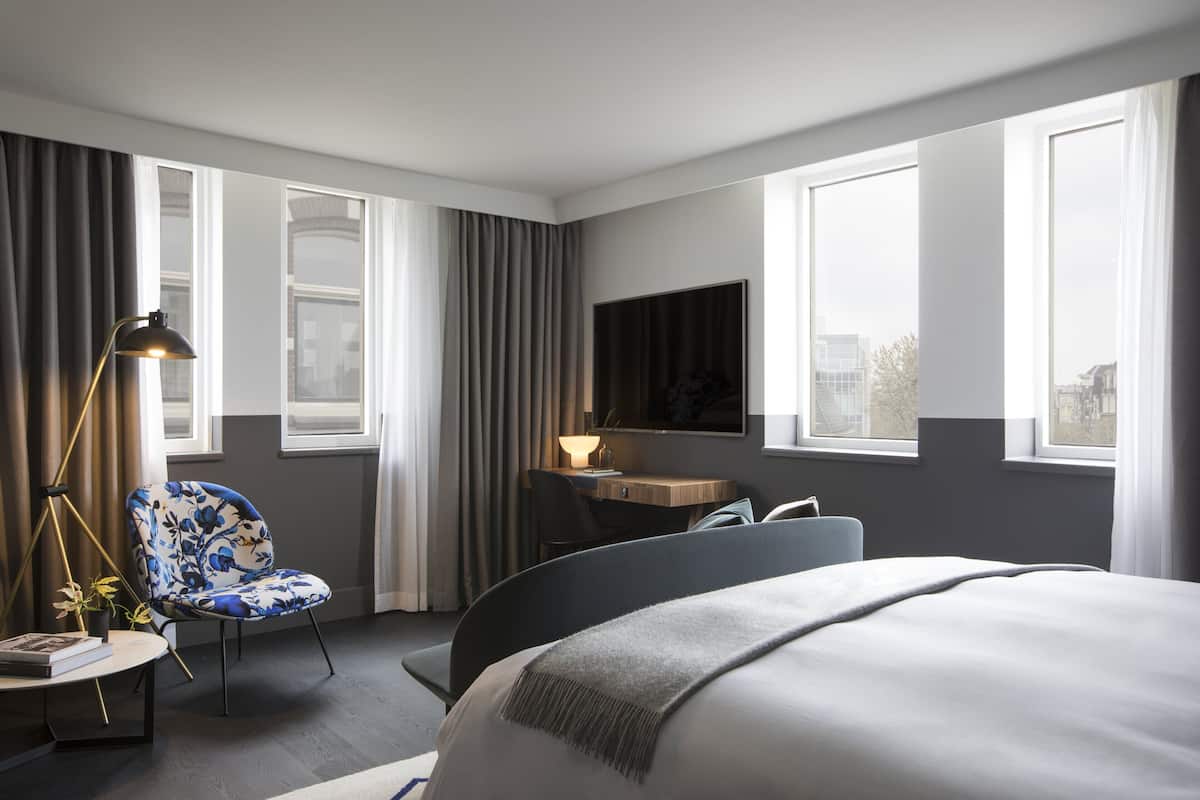 Ein Hotelzimmer mit einem Bett, einem Schreibtisch mit Stuhl, einem Fernseher und großen Fenstern.