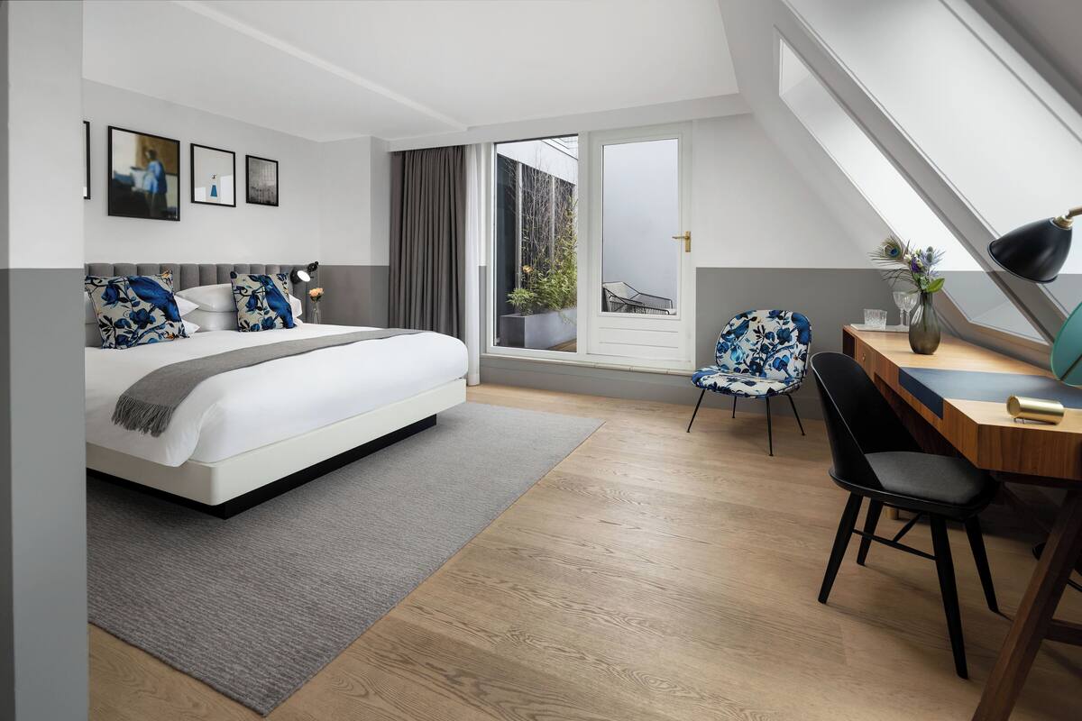 Ein modernes Schlafzimmer mit einem großen Bett, einem Schreibtisch und einem Stuhl. Ein Fenster bietet einen Ausblick nach draußen.