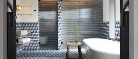 A bathroom with a geometric patterned floor, a wooden stool, a white bathtub, and a sink with a towel rack.