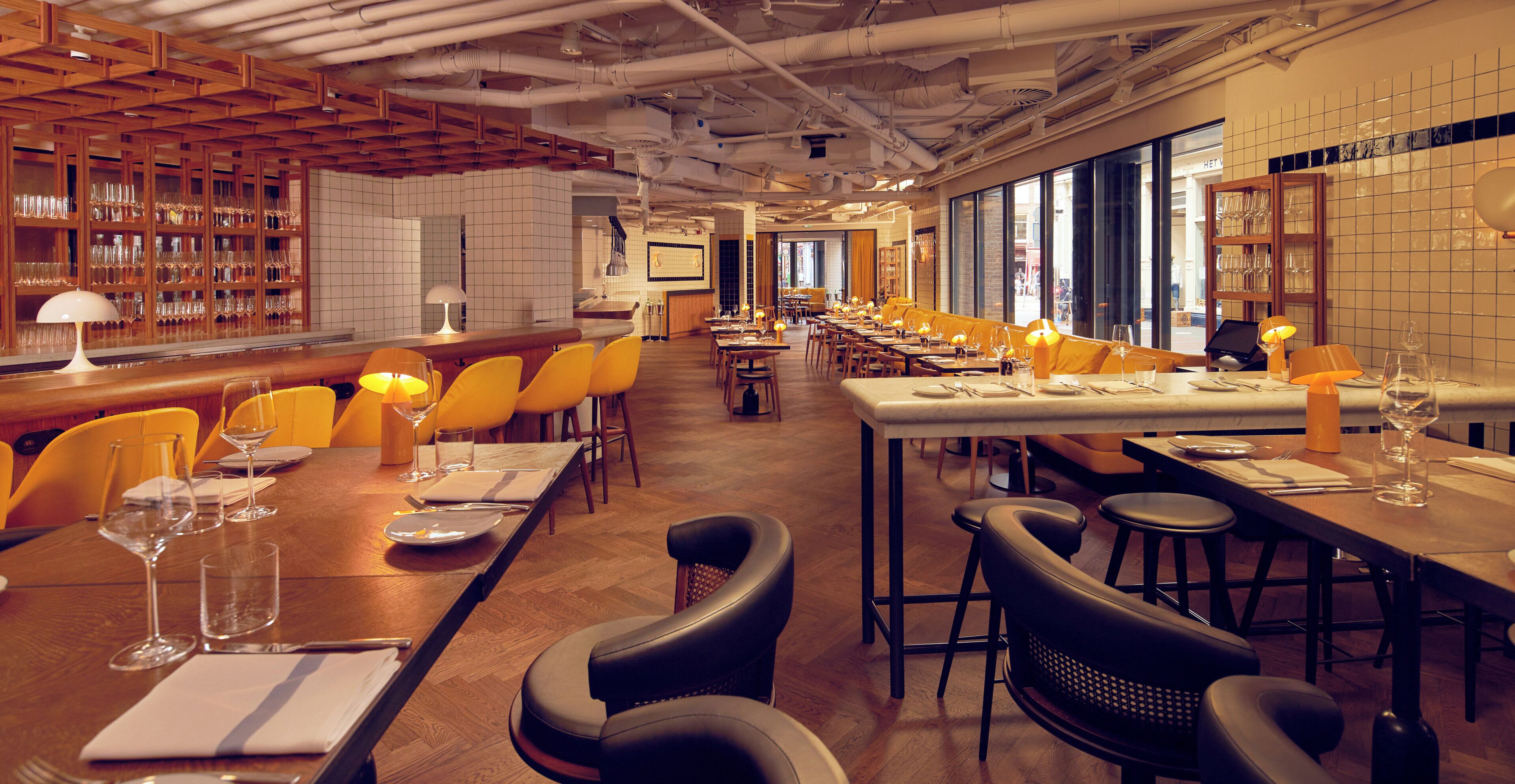 A restaurant with multiple dining tables, chairs, and a bar area with shelves of glasses.