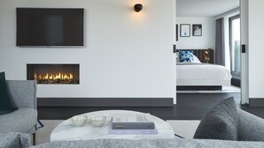 Una habitación de hotel moderna con una televisión de pantalla plana, chimenea, cama con cabecera y un ventanal grande.