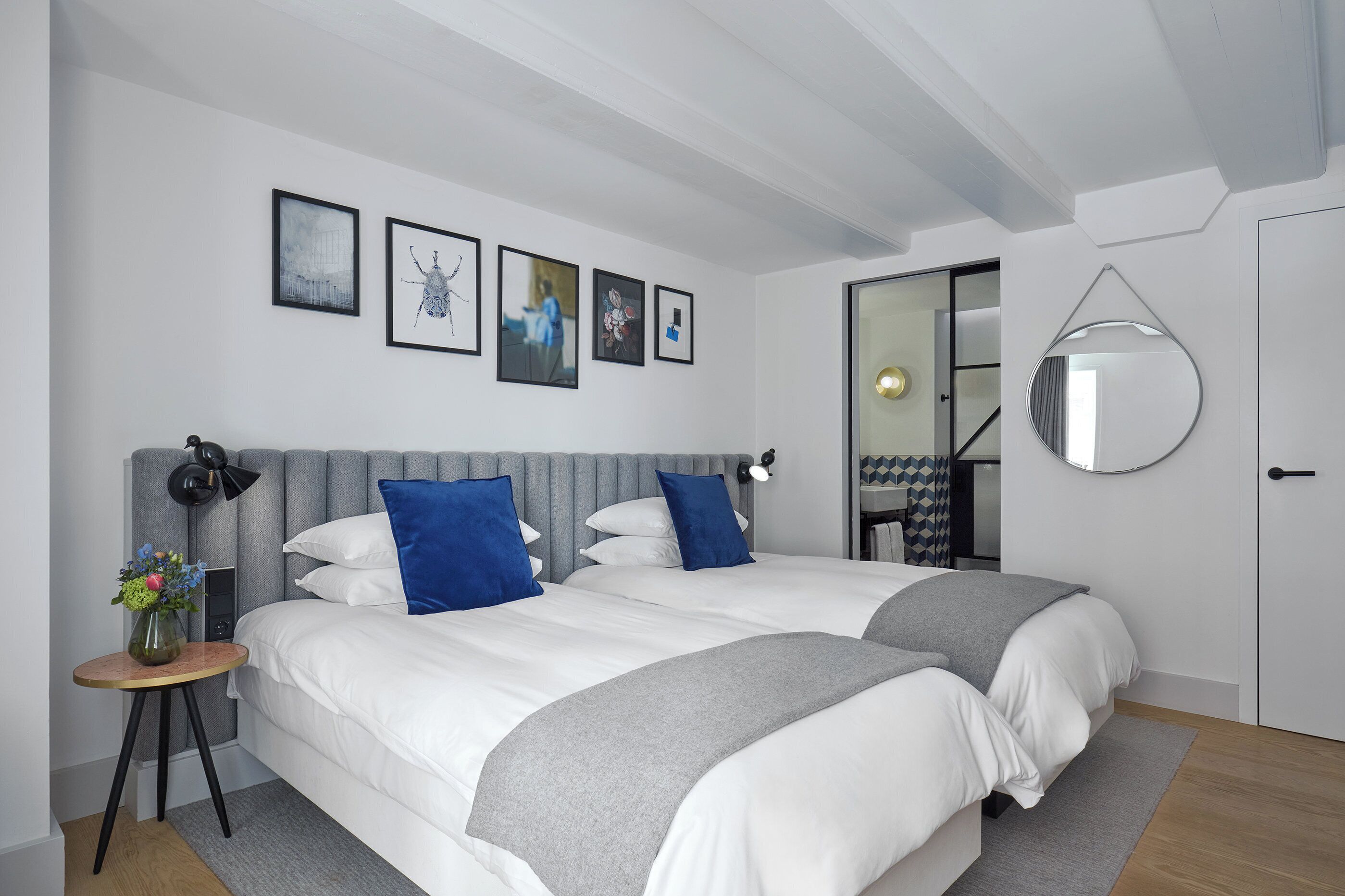 Ein modernes Schlafzimmer mit zwei Betten, einem runden Spiegel und Bildern an der Wand.