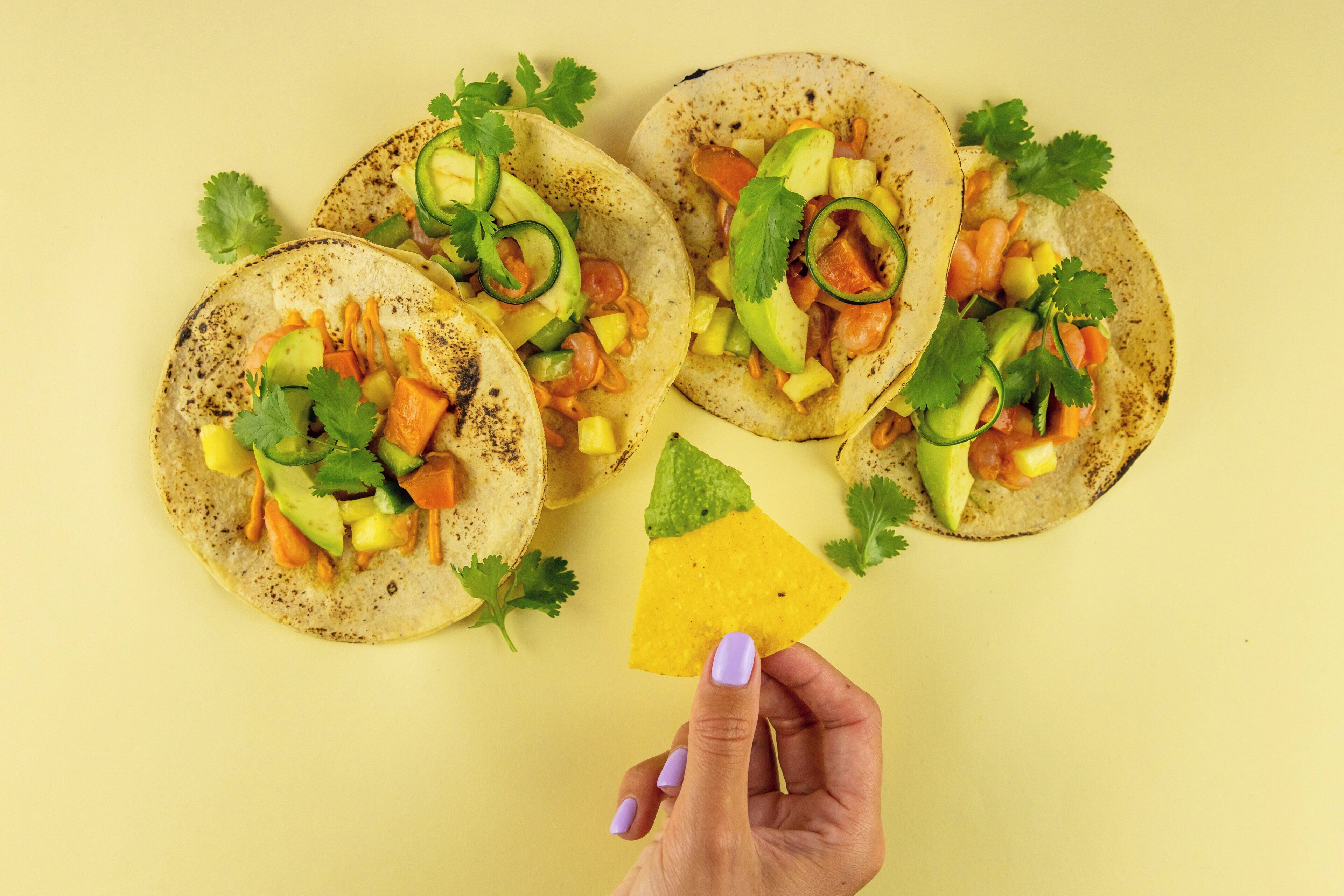 A hand holding a tortilla with a yellow tortilla chip.