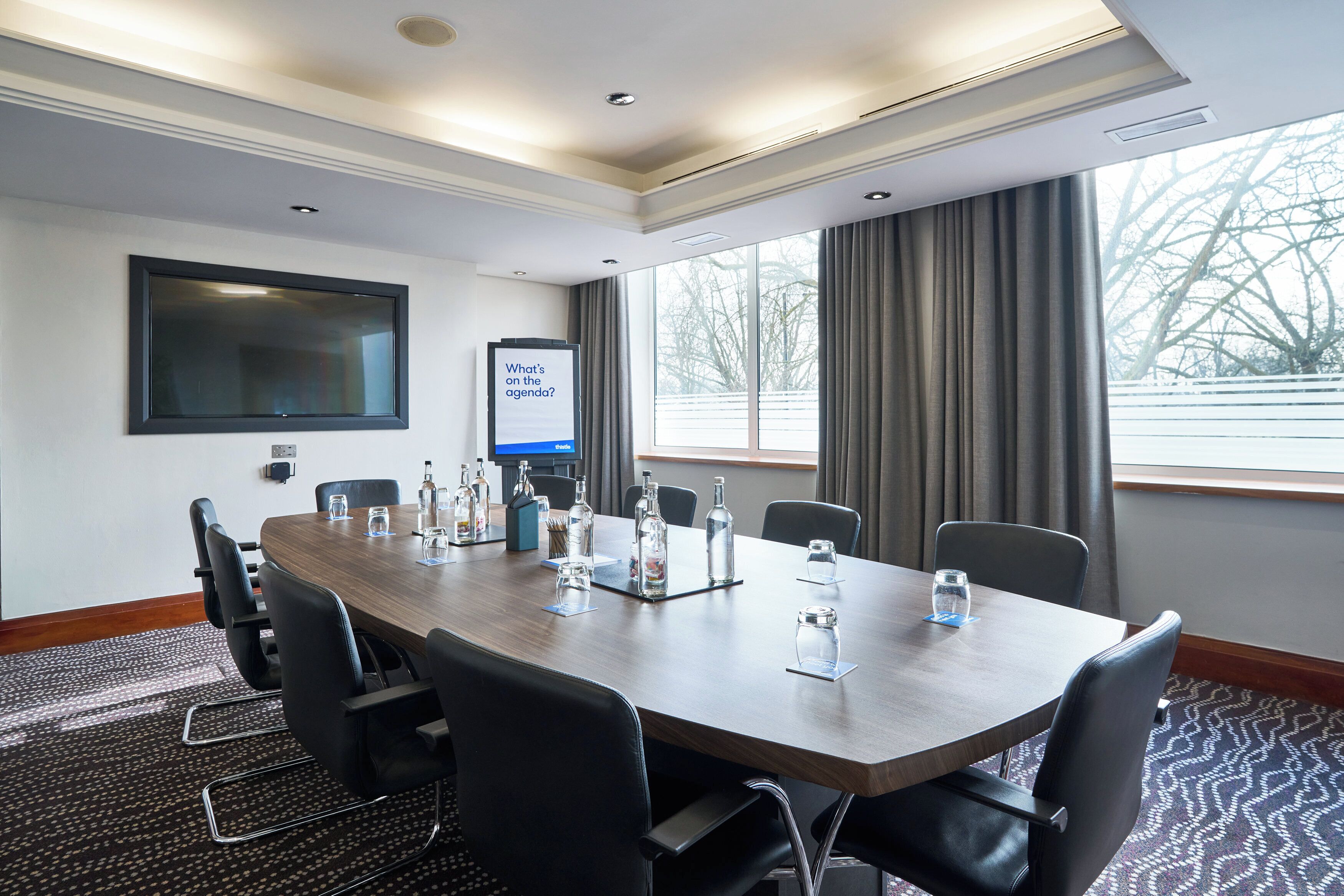 A conference room with a long table, chairs, a screen, and a projector.